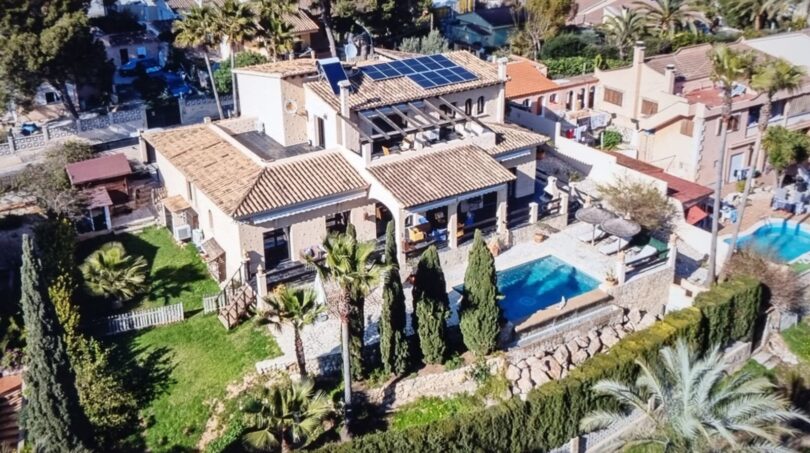 Vista aérea de una villa mediterránea con piscina, paneles solares, terraza y jardín exuberante en Costa de la Calma
