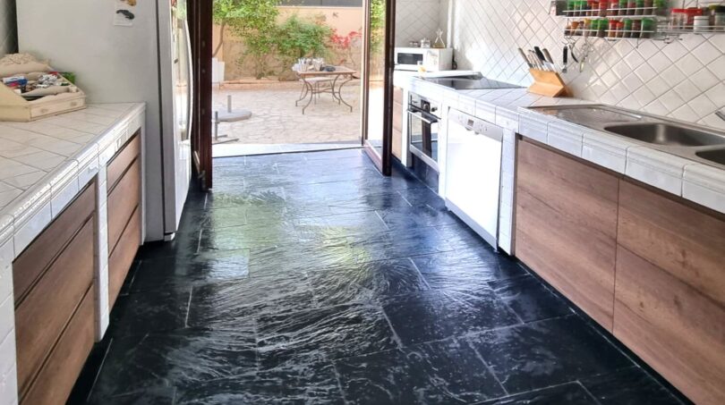 Espaciosa cocina de la villa en Calvia con suelo de piedra natural oscura, frentes de madera y acceso a la terraza.