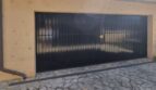 Garaje doble con puerta de lamas negra, pavimento de piedra natural y techo de tejas de terracota mediterránea de la villa en Costa de la Calma