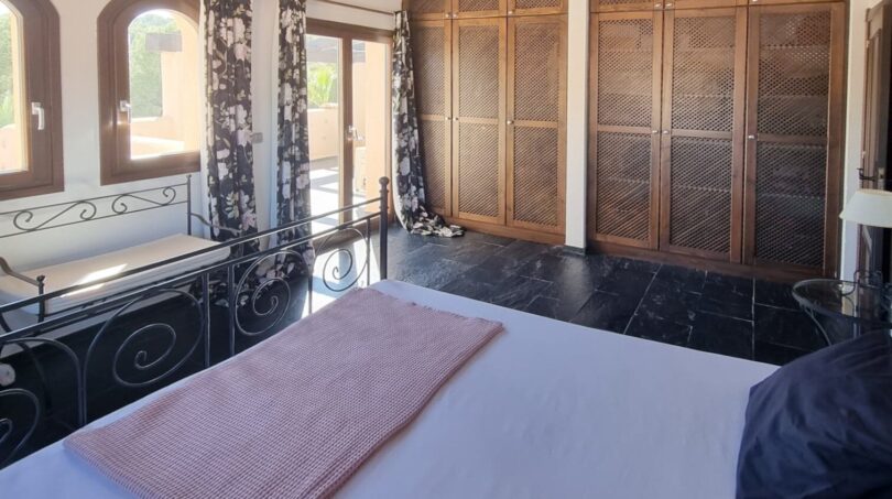 Dormitorio luminoso de la villa en Calvia con techo de vigas de madera, gran armario empotrado y elegante cama de metal.