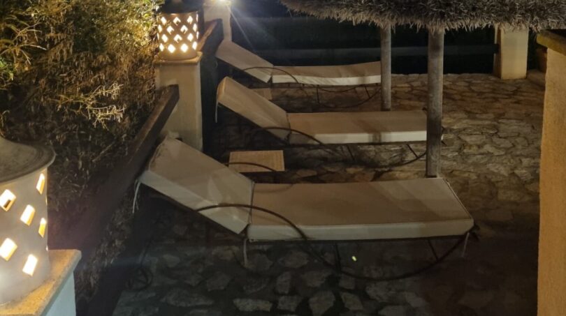 Terraza de piscina iluminada de la villa por la noche con tumbonas, sombrillas de paja y linternas decorativas