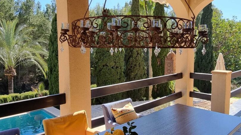 Terraza cubierta con araña de hierro forjado, mesa de comedor y vistas a la piscina, Villa Calvia