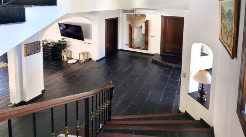 Elegante vestíbulo de entrada con suelo de piedra natural negra, escalera de madera y barandilla de hierro forjado en villa exclusiva en Calvia.