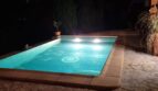 Piscina iluminada de noche con borde de piedra natural y palapa, villa en Costa de la Calma