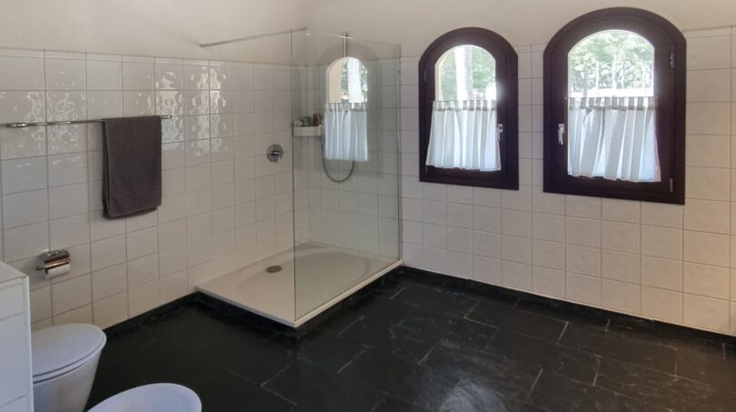 Baño luminoso de la villa con ducha, bidé, suelo de piedra natural oscura y techo de vigas de madera