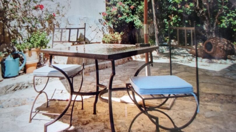 Terraza soleada con muebles de hierro forjado, sombrilla y exuberante vegetación de la villa en Costa de la Calma.
