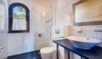 Baño luminoso de la villa en Calvià con ducha, lavabo tipo recipiente, WC y ventana de arco redondo