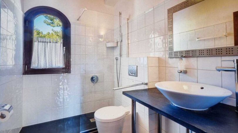 Baño luminoso de la villa en Calvià con ducha, lavabo tipo recipiente, WC y ventana de arco redondo