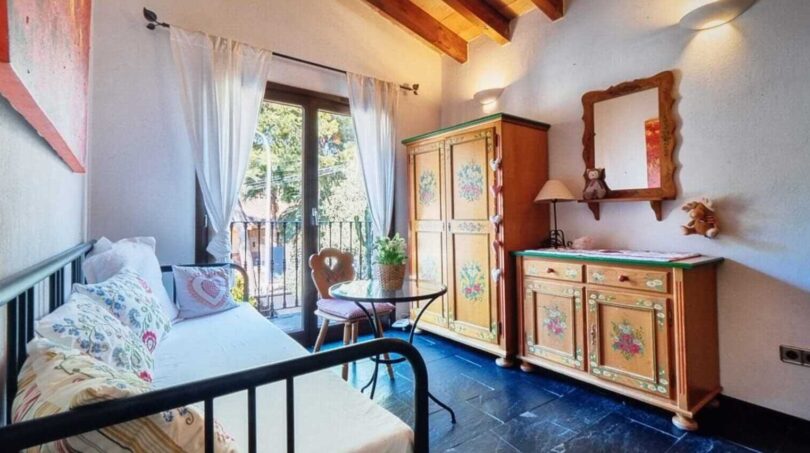 Acogedor dormitorio de la villa en Calvià con armario de madera pintada, techo de vigas de madera y balcón con vistas al jardín.