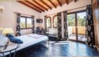 Dormitorio luminoso de la villa en Calvià con techo de vigas de madera, acceso a terraza y vistas a las palmeras