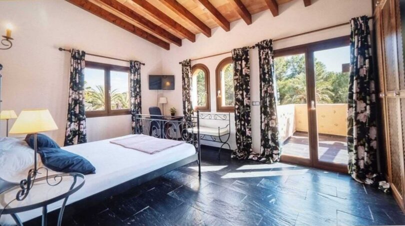 Dormitorio luminoso de la villa en Calvià con techo de vigas de madera, acceso a terraza y vistas a las palmeras