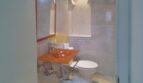 Modernes Bad der Hafenwohnung Palma mit orangefarbenem Waschbecken, weißem WC und eleganter Marmorverkleidung.