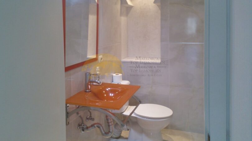 Modernes Bad der Hafenwohnung Palma mit orangefarbenem Waschbecken, weißem WC und eleganter Marmorverkleidung.