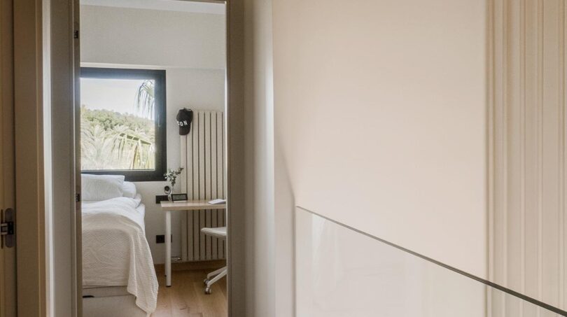 Heller Flur mit Holzboden führt zu modernem Schlafzimmer mit Schreibtisch und Gartenblick