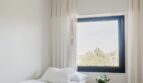 Helles Schlafzimmer der Maisonette mit weißer Bettwäsche, elegantem Nachttisch und Fenster mit Palmblick