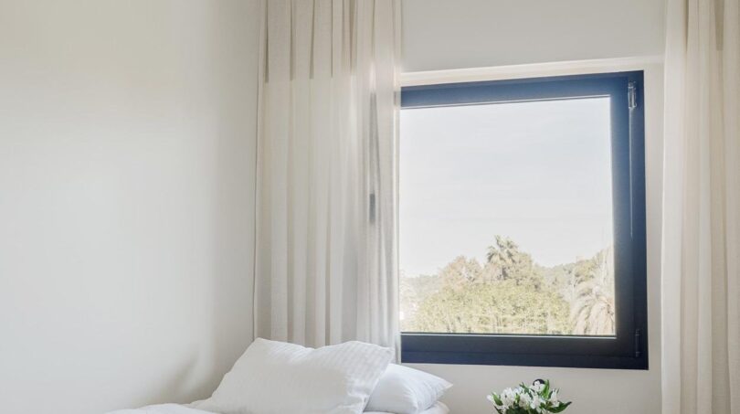 Helles Schlafzimmer der Maisonette mit weißer Bettwäsche, elegantem Nachttisch und Fenster mit Palmblick