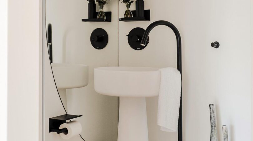 Elegantes Designer-Badezimmer mit Säulenwaschbecken, schwarzen Akzenten und großem Rundbogenspiegel