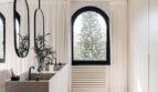 Elegantes Badezimmer der Maisonette mit Designspiegel, Naturstein-Waschtisch und Bogenfenster mit Meerblick