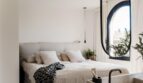 Helles Schlafzimmer der Maisonette mit Leinenbettwäsche, ovalem Fenster und elegantem Waschtisch