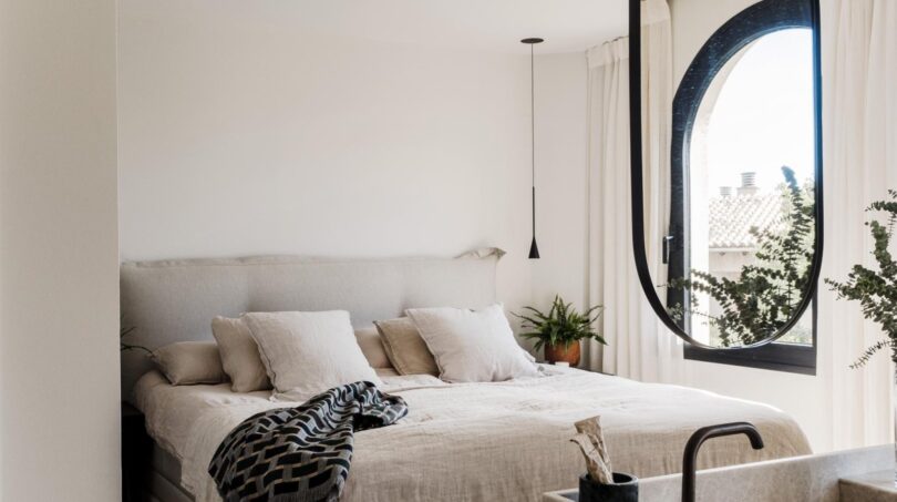Helles Schlafzimmer der Maisonette mit Leinenbettwäsche, ovalem Fenster und elegantem Waschtisch