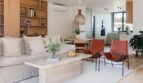 Helles Wohnzimmer mit Leinensofa, Ledersessel, Holzregal und offener Küche in Maisonette Palma