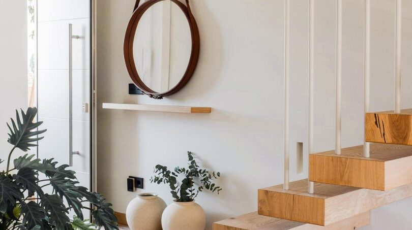 Helles Treppenhaus der Maisonette mit schwebender Holztreppe, rundem Spiegel und Monstera-Pflanze
