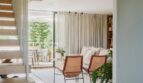 Offener Wohnbereich der Maisonette mit Designstühlen, Holztreppe und Glasgeländer sowie Terrassenzugang