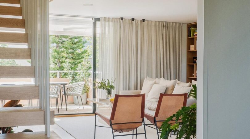 Offener Wohnbereich der Maisonette mit Designstühlen, Holztreppe und Glasgeländer sowie Terrassenzugang