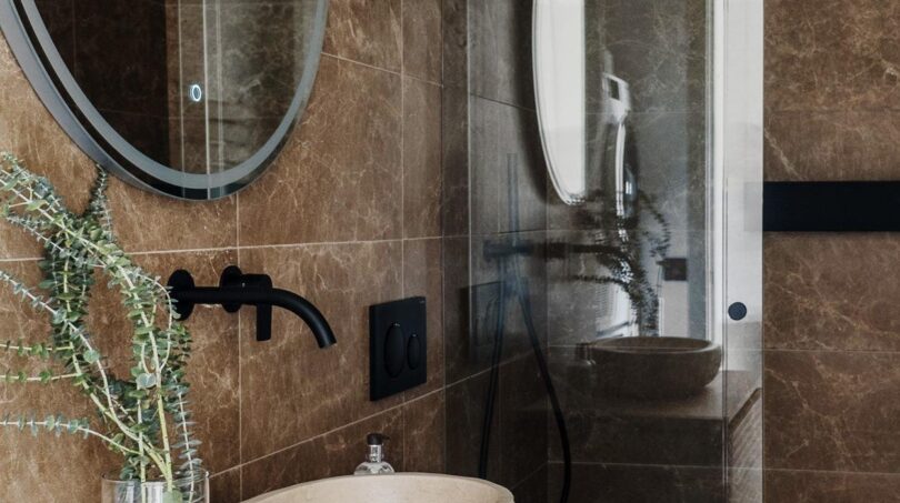 Luxuriöses Badezimmer mit Marmorwänden, Naturstein-Waschbecken, Holzwaschtisch und Glasdusche