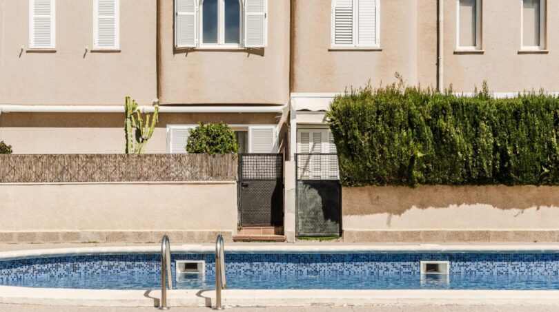 Außenpool mit Edelstahlleiter vor mediterranem Wohnhaus mit weißen Fensterläden und gepflegter Begrünung in Palma