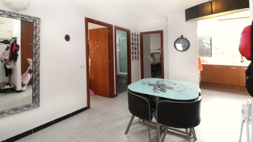Heller Essbereich mit modernem Glastisch, schwarzen Stühlen, Spiegel und Blick in Bad und Schlafzimmer