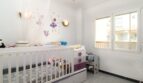 Kinderzimmer mit weißem Gitterbett, Kommode in Lila-Weiß, Feensticker an der Wand und Fenster mit Ausblick.