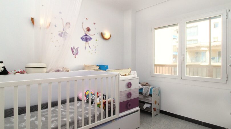 Kinderzimmer mit weißem Gitterbett, Kommode in Lila-Weiß, Feensticker an der Wand und Fenster mit Ausblick.