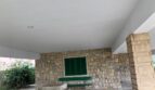 Überdachte Terrasse mit Natursteinwand, grünen Fensterläden und Hochbeeten in Alcúdia, nahe dem Strand.