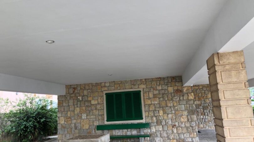 Überdachte Terrasse mit Natursteinwand, grünen Fensterläden und Hochbeeten in Alcúdia, nahe dem Strand.