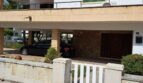 Zweistöckige Villa in Alcúdia mit Carport, grünen Fensterläden und gepflasterter Einfahrt, strandnah gelegen.