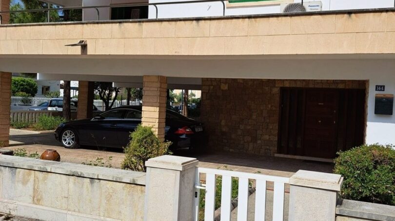 Zweistöckige Villa in Alcúdia mit Carport, grünen Fensterläden und gepflasterter Einfahrt, strandnah gelegen.
