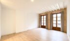 Helles Wohnzimmer der Maisonette in Palma mit Holzboden, Steinwand, Deckenbalken und französischen Fenstertüren.