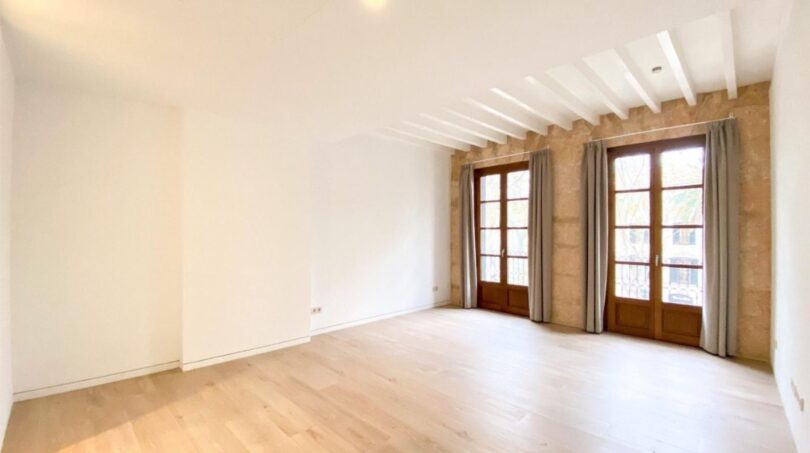 Helles Wohnzimmer der Maisonette in Palma mit Holzboden, Steinwand, Deckenbalken und französischen Fenstertüren.