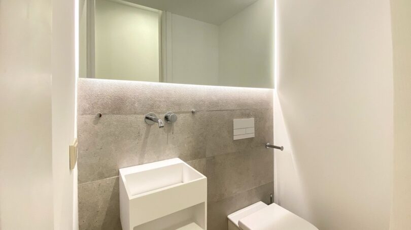 Modernes Gäste-WC der Maisonette in Palma mit beleuchtetem Spiegel, Wandarmatur und schwebender Toilette.