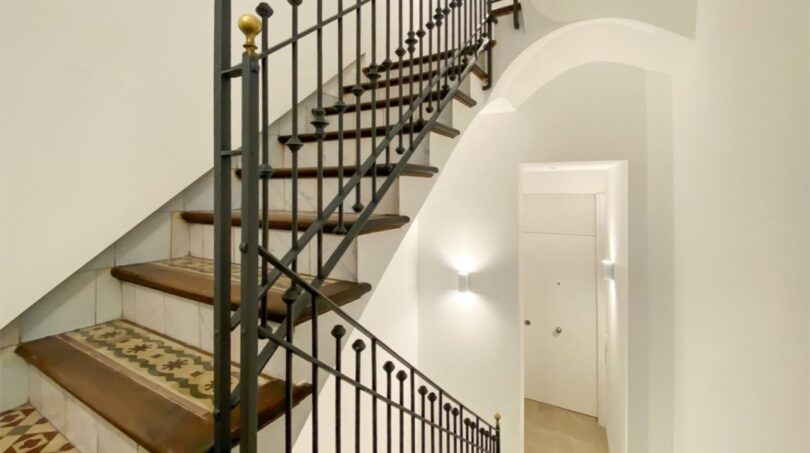 Elegantes Treppenhaus der Maisonette in Palma mit schmiedeeisernem Geländer und historischen Mosaikfliesen.