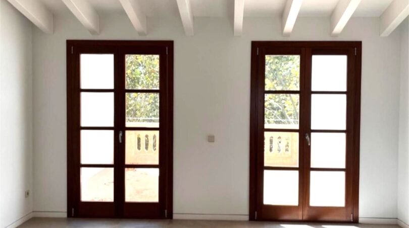 Heller Wohnraum mit zwei Holz-Terrassentüren, weißen Balkendecken und Natursteinboden in Maisonette-Wohnung, Palma