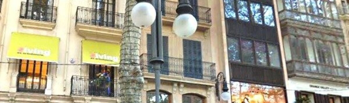 Außenansicht eines eleganten Altbaus in belebter Einkaufsstraße in Palma de Mallorca mit klassischer Fassade und Balkonen.