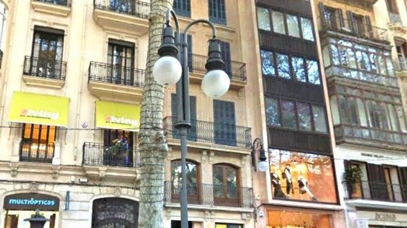 Außenansicht eines eleganten Altbaus in belebter Einkaufsstraße in Palma de Mallorca mit klassischer Fassade und Balkonen.