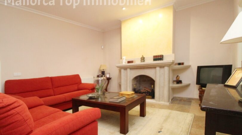 Wohnzimmer der Villa in Alcúdia mit roten Sofas, Steinkamin und TV-Bereich.