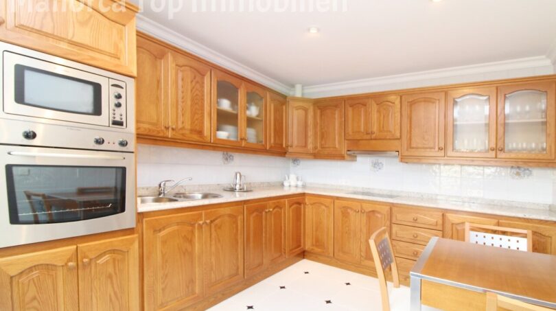 Geräumige Küche der Villa in Alcúdia mit Holzschränken, Einbauofen, Mikrowelle und Esstisch.