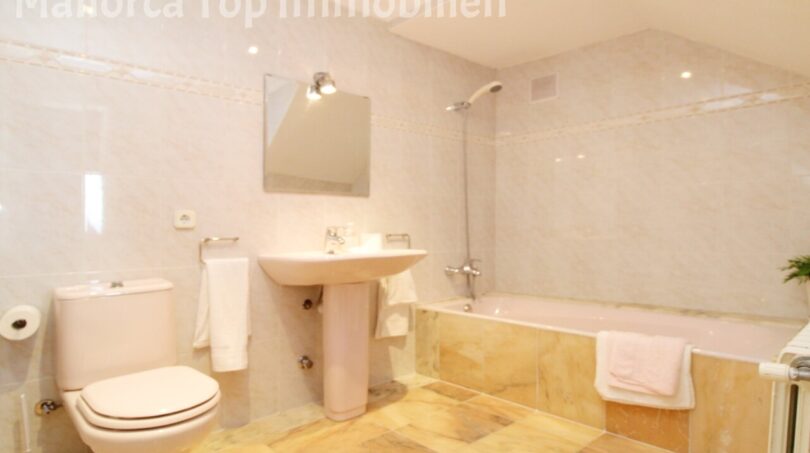 Helles Badezimmer der Villa in Alcúdia mit Badewanne, Dusche, Waschbecken und beigen Fliesen.