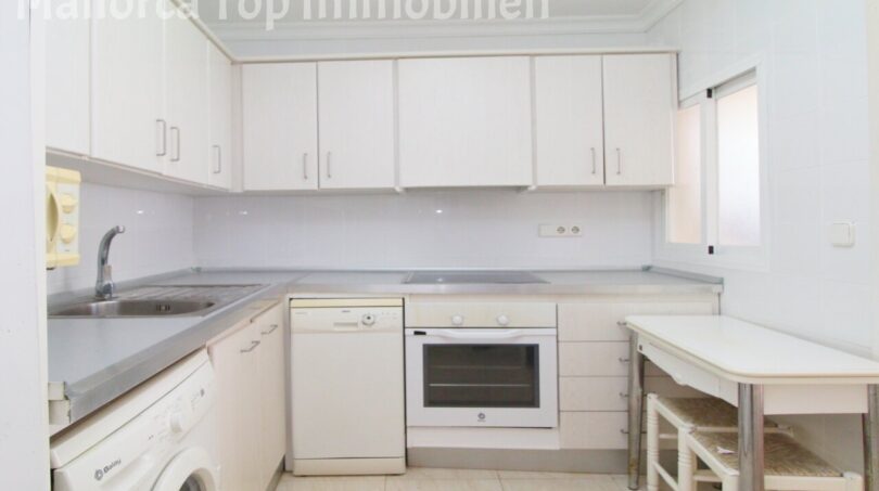 Helle weiße Küche der Villa in Alcúdia mit Einbaugeräten, Waschmaschine und kleinem Esstisch.