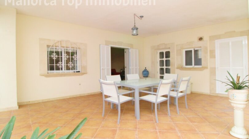 Überdachte Terrasse der Villa in Alcúdia mit Esstisch, Terrakottaboden und Blick ins Innere.