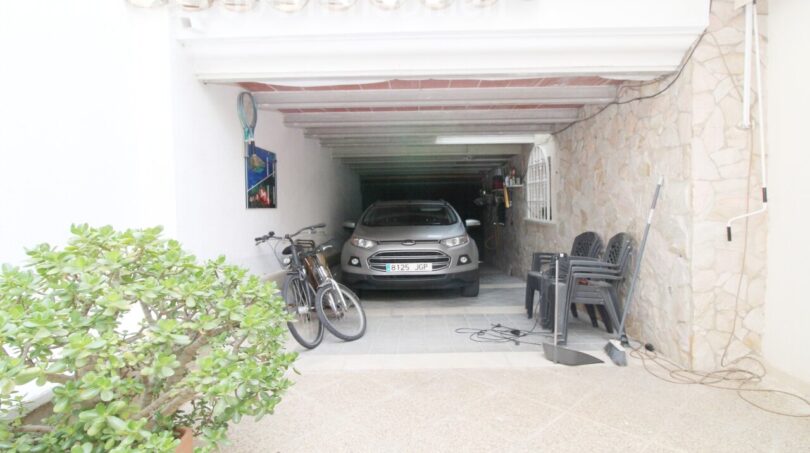 Überdachte Garage der Villa in Alcúdia mit PKW, Fahrrädern und Natursteinwand, nahe Hafen.